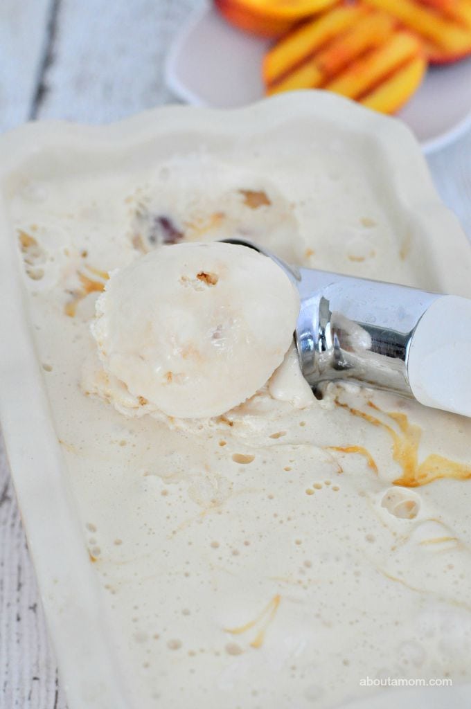 Grilled peach ice cream with caramel swirls being scooped from a white loaf pan.