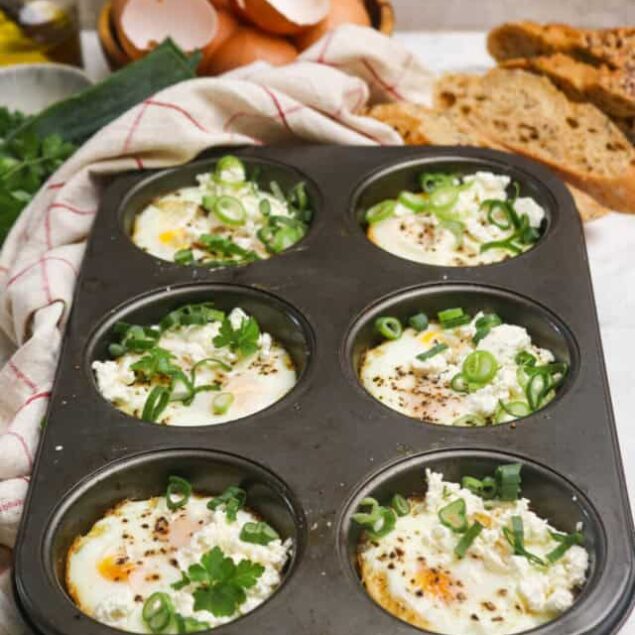 Perfect baked eggs in a muffin tin, topped with feta cheese, green onions, and parsley.