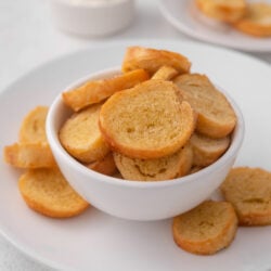 Golden-brown bagel chips in a white bowl, served with a creamy dip.