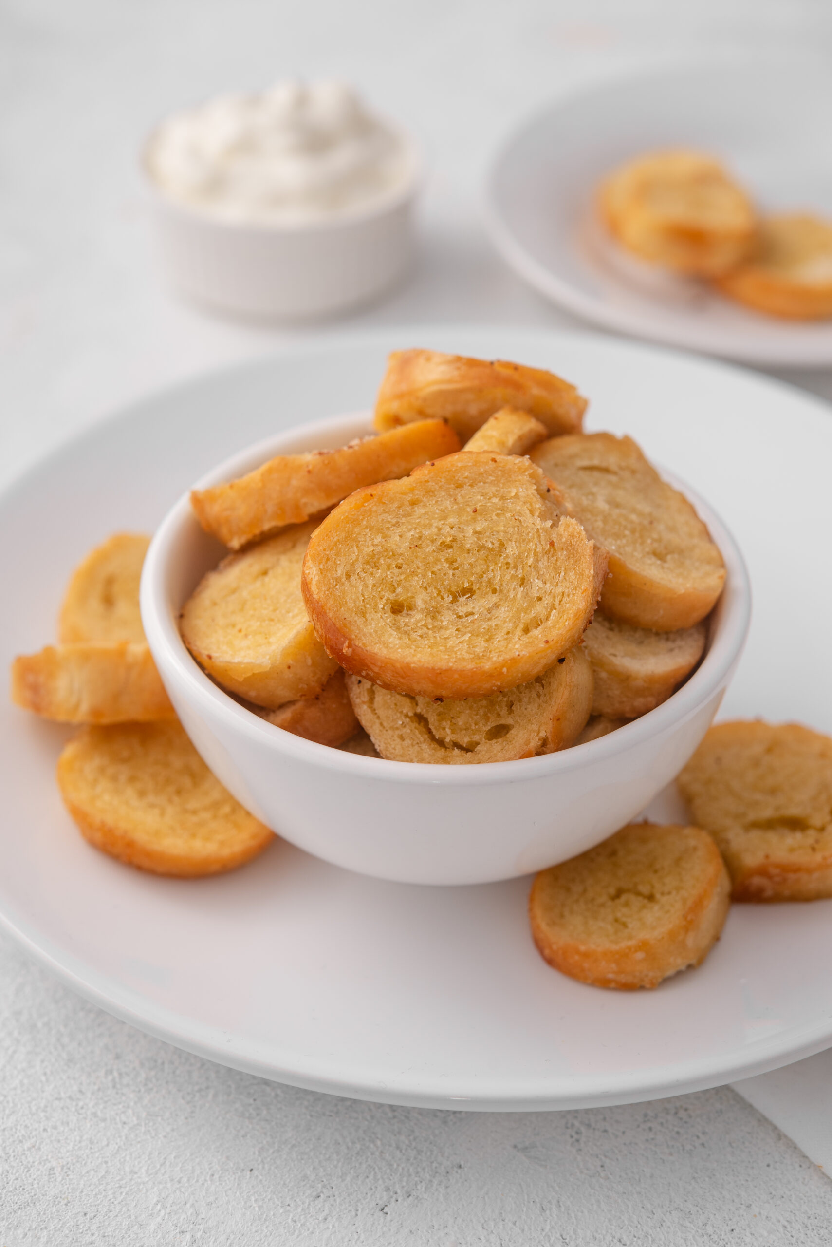 Golden-brown bagel chips in a white bowl, served with a creamy dip.