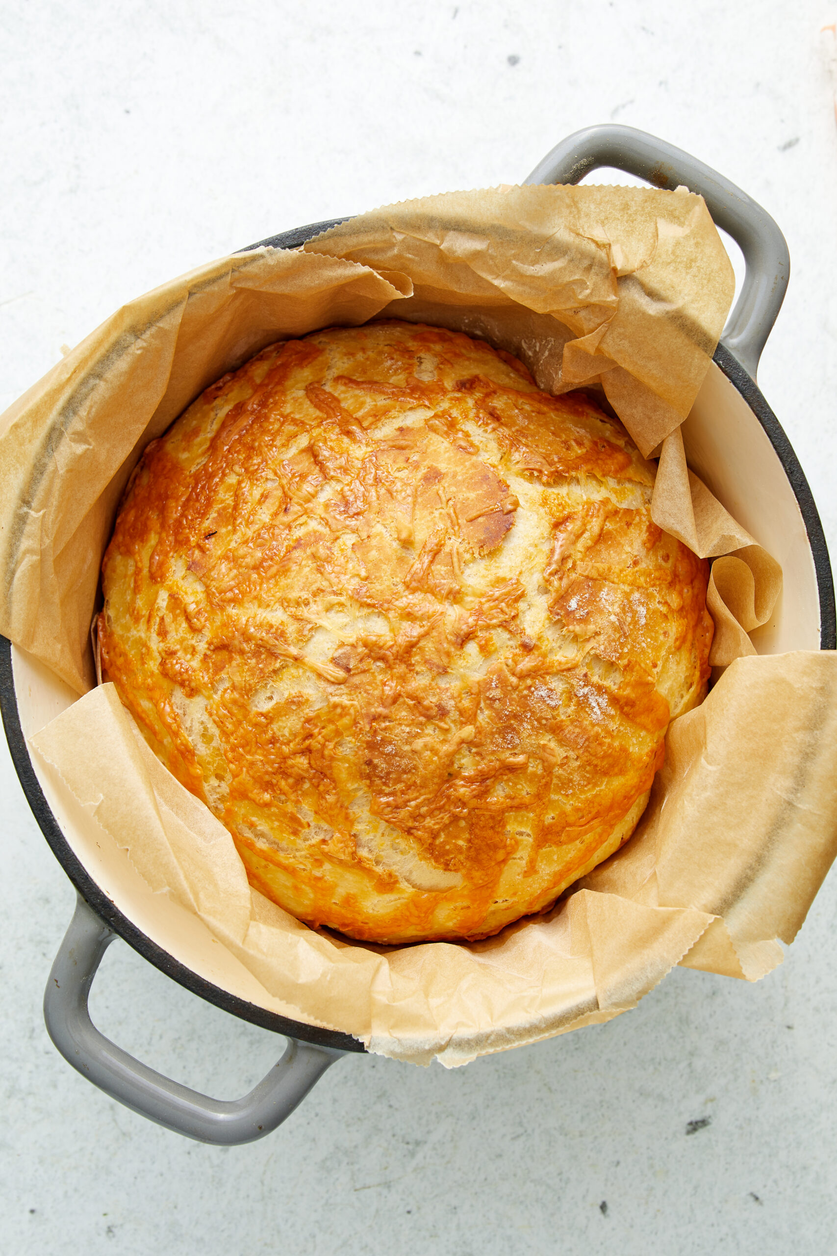 A golden-brown loaf of Cheese Bread in a Dutch oven, lined with parchment paper.