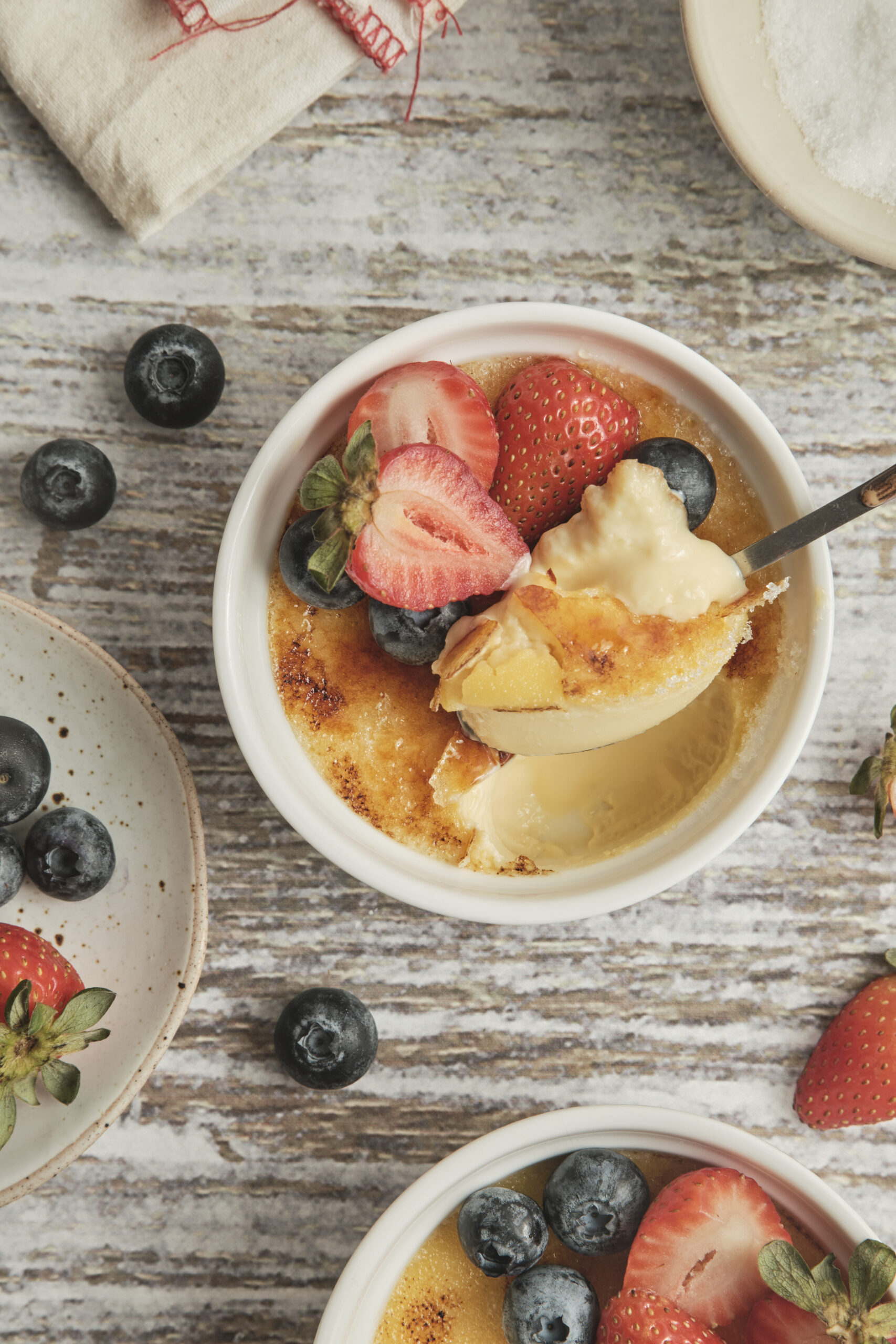 Cr&egrave;me br&ucirc;l&eacute;e with a caramelized sugar crust, garnished with fresh strawberries and blueberries.