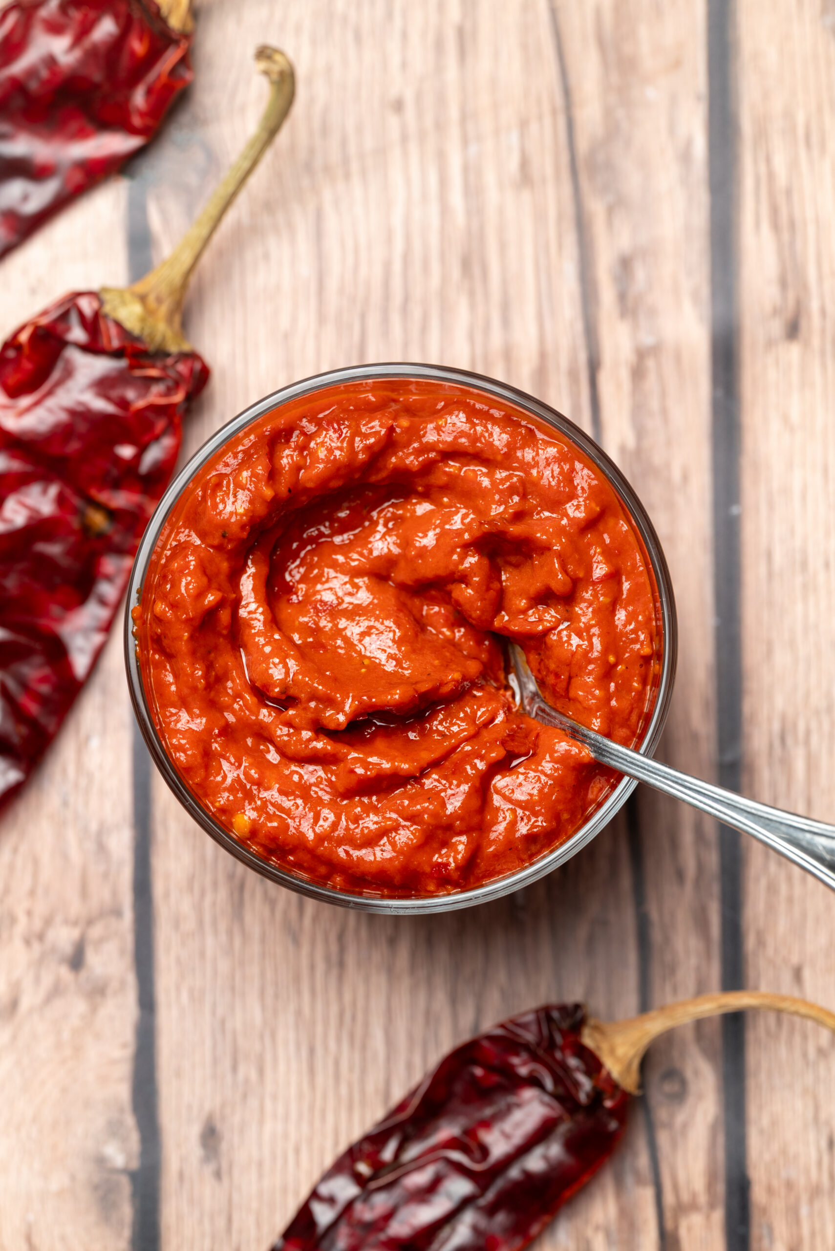 Homemade harissa paste in a glass bowl with a spoon, surrounded by dried red chiles.