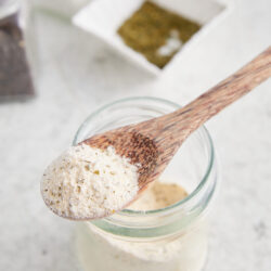 Homemade Ranch Seasoning in a glass jar, with a wooden spoon scooping some out.