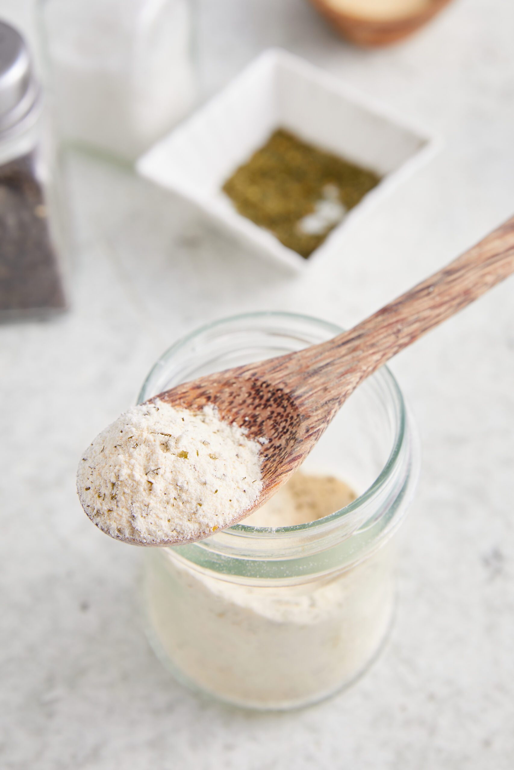 Homemade Ranch Seasoning in a glass jar, with a wooden spoon scooping some out.