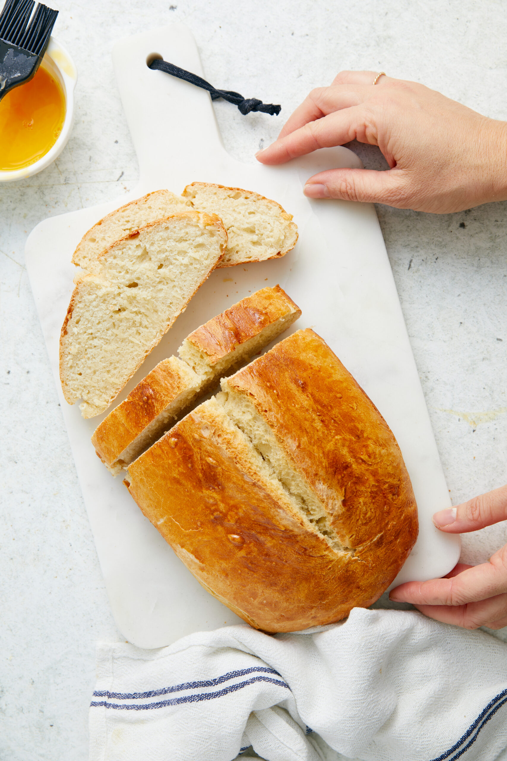 Partially sliced Italian bread on a white cutting board, held by a person's hands.