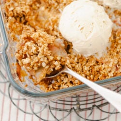 A serving of peach crisp with a golden oat topping and melting vanilla ice cream.