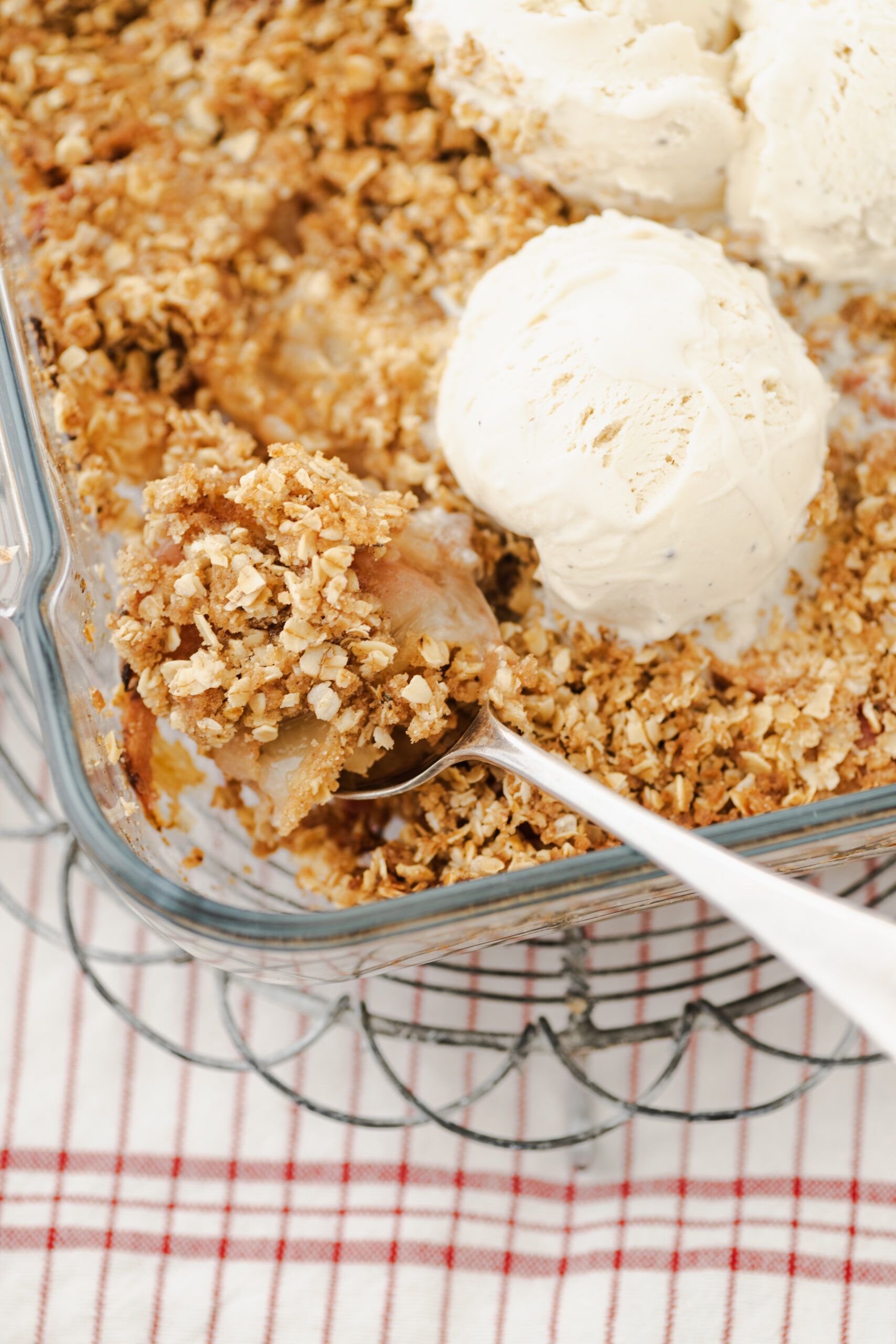 A serving of peach crisp with a golden oat topping and melting vanilla ice cream.