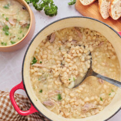 Senate bean soup in a red Dutch oven and a small bowl, garnished with fresh parsley.