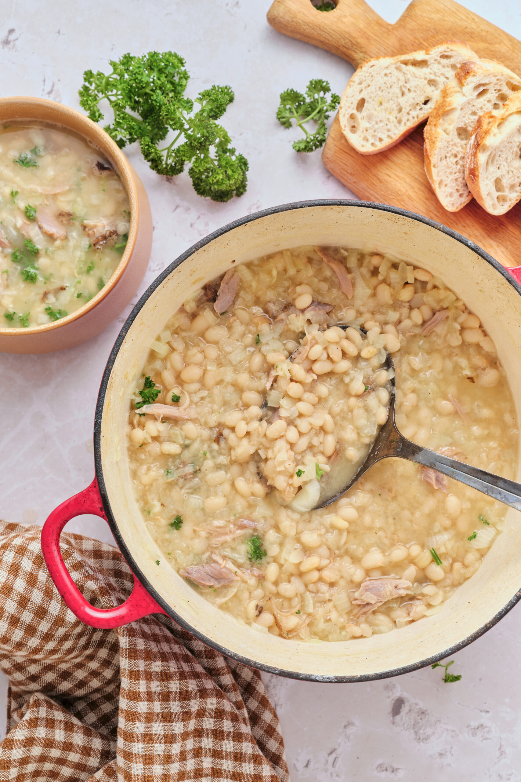 Senate bean soup in a red Dutch oven and a small bowl, garnished with fresh parsley.