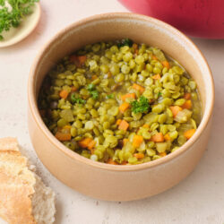 Vegan Split Pea Soup in a beige bowl, garnished with parsley, served with crusty bread.