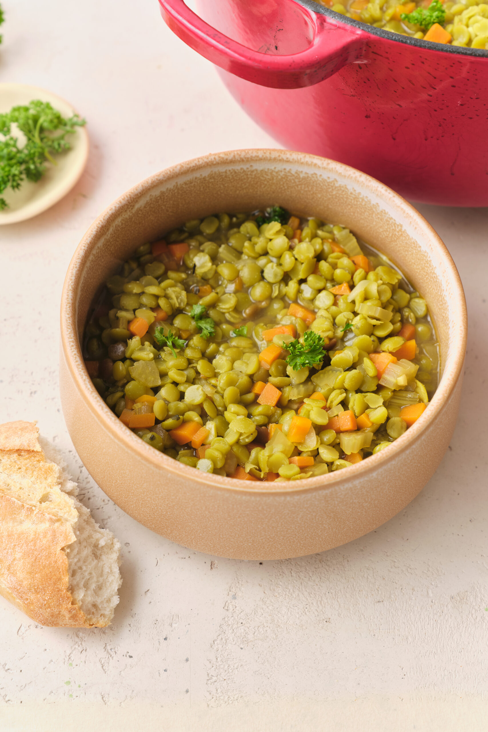 Vegan Split Pea Soup in a beige bowl, garnished with parsley, served with crusty bread.