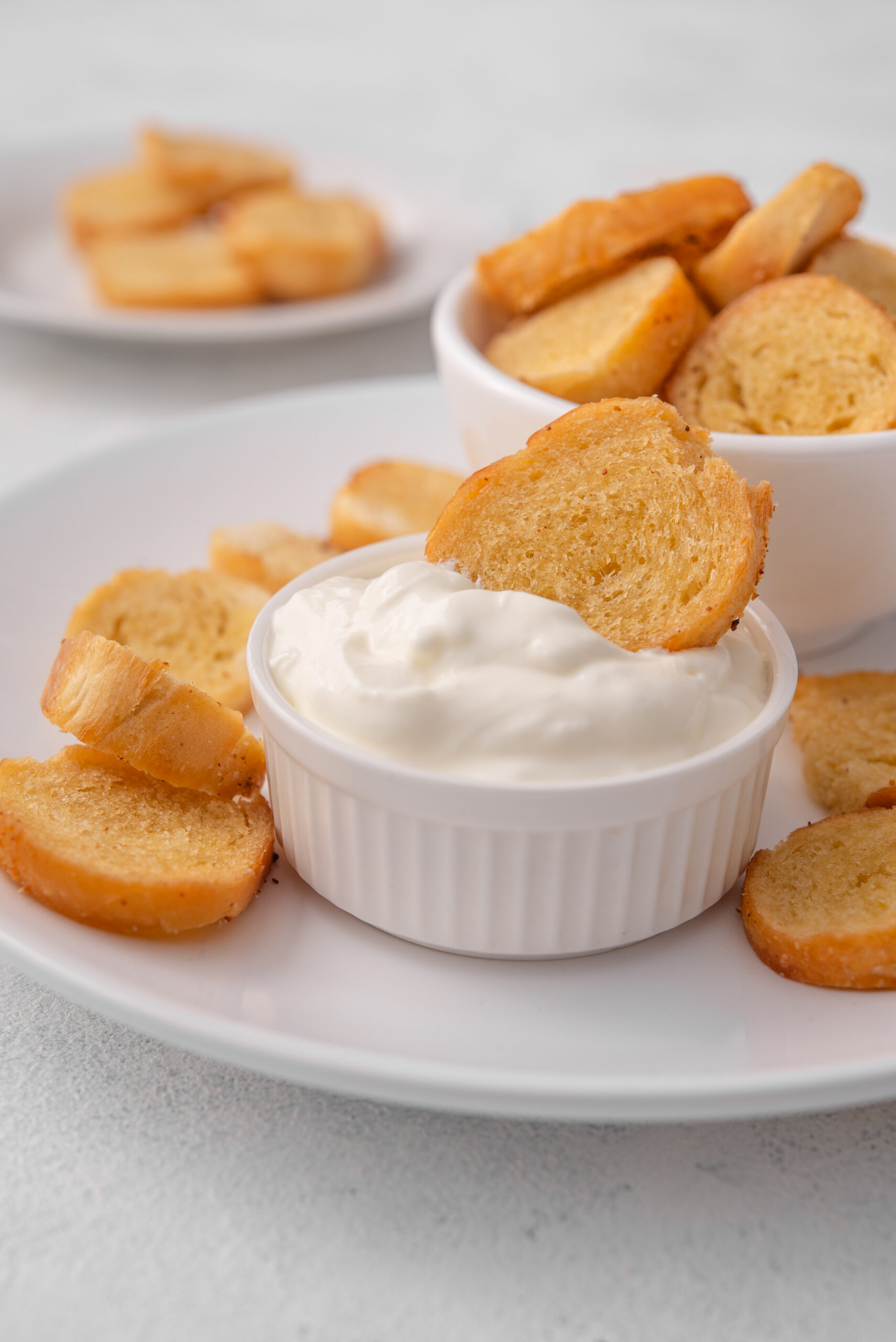 Golden-brown bagel chips served on a white plate with a creamy white dip.