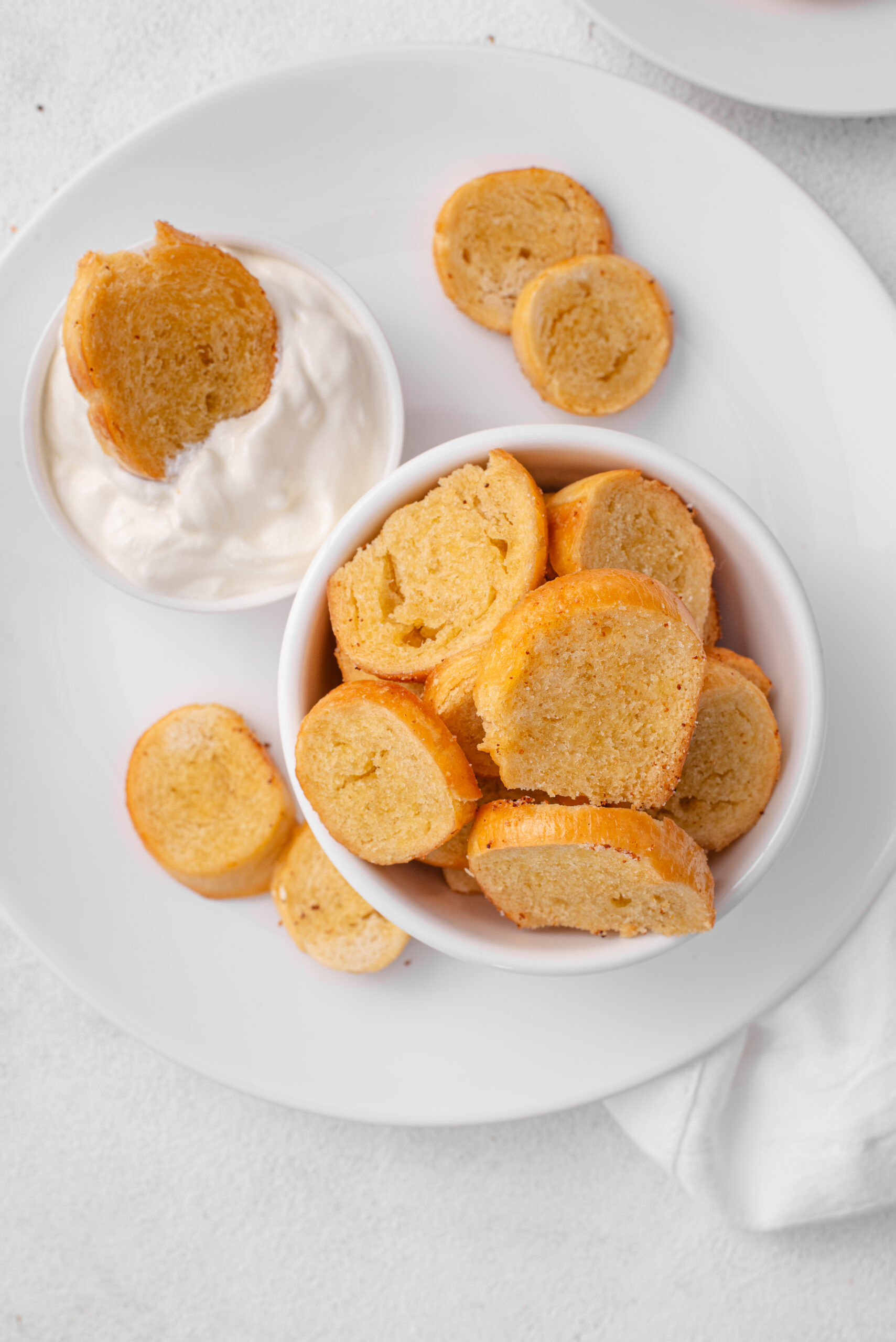 Golden-brown Bagel Chips served in a white bowl with a side of creamy dip.