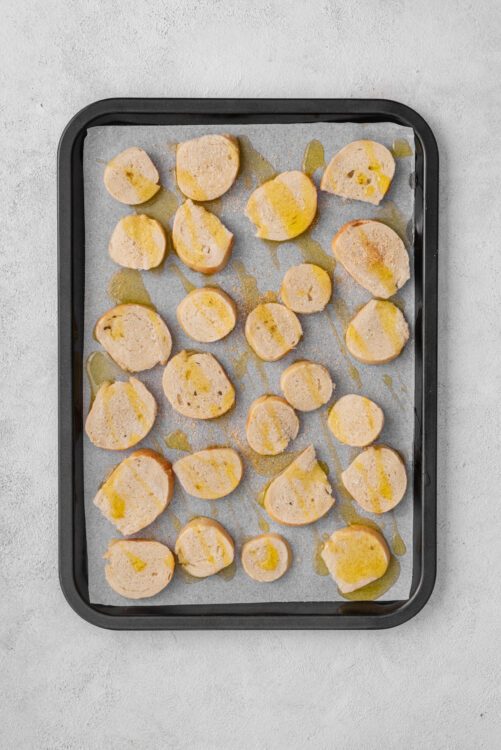 Bagel chips slices drizzled with olive oil on a baking sheet.