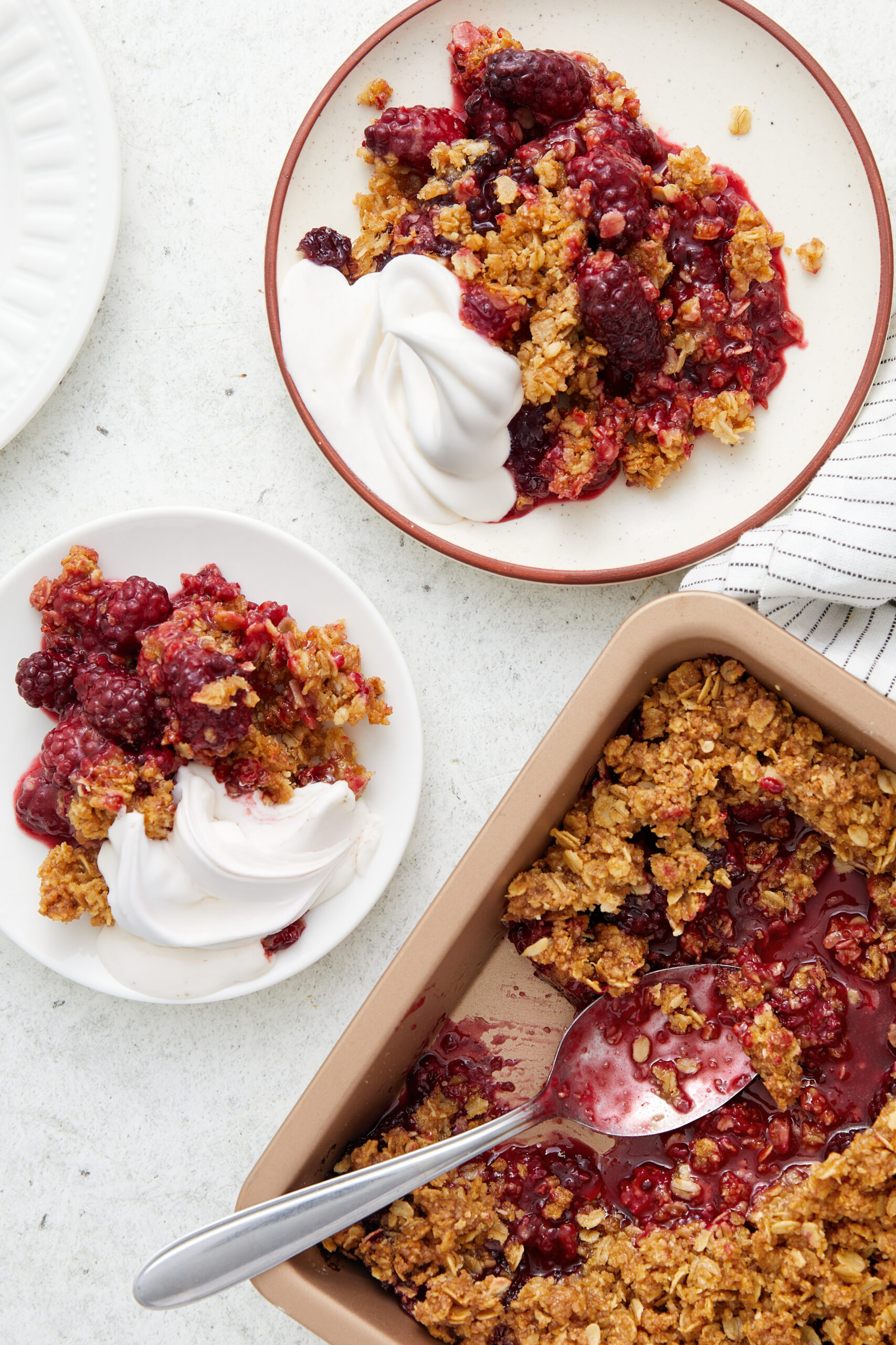 Blackberry crisp in a baking dish and served on plates with whipped cream.
