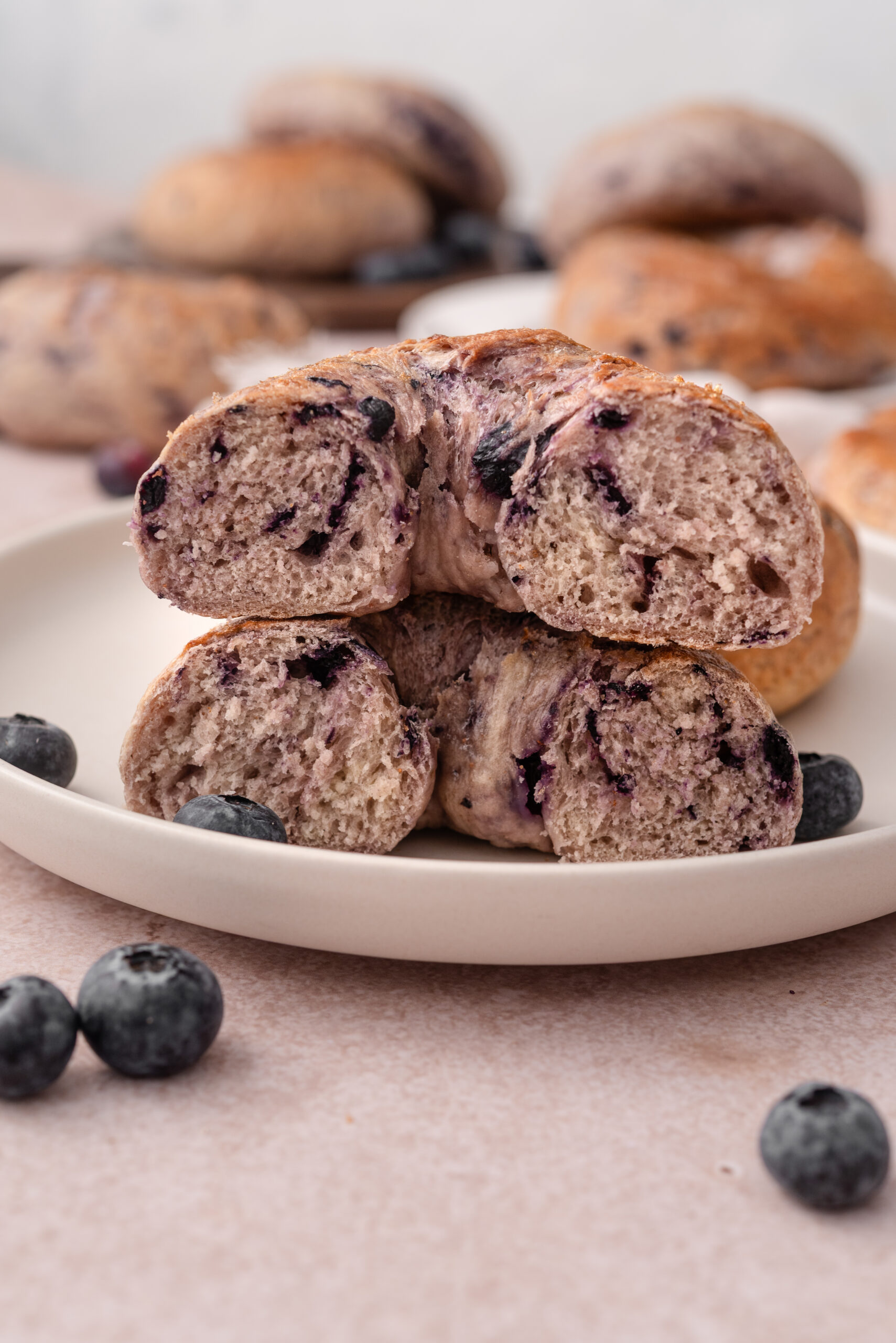 Blueberry bagel cut in half and stacked on a white plate, with fresh blueberries.