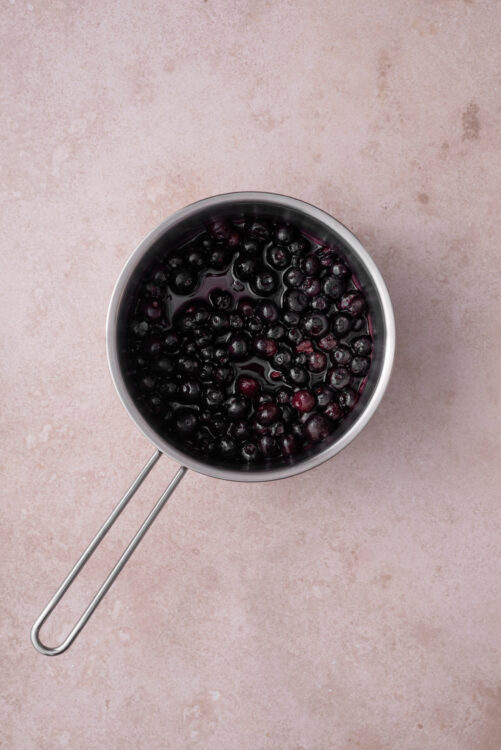 Warming blueberries in a small saucepan for blueberry bagels.