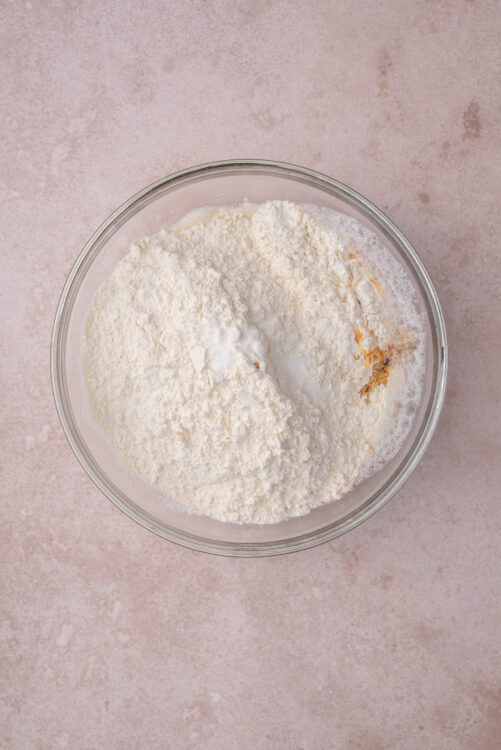 Adding bread flour, salt, and vanilla extract to the yeast mixture for blueberry bagels.