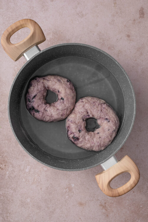 Boiling blueberry bagels in a pot of water.