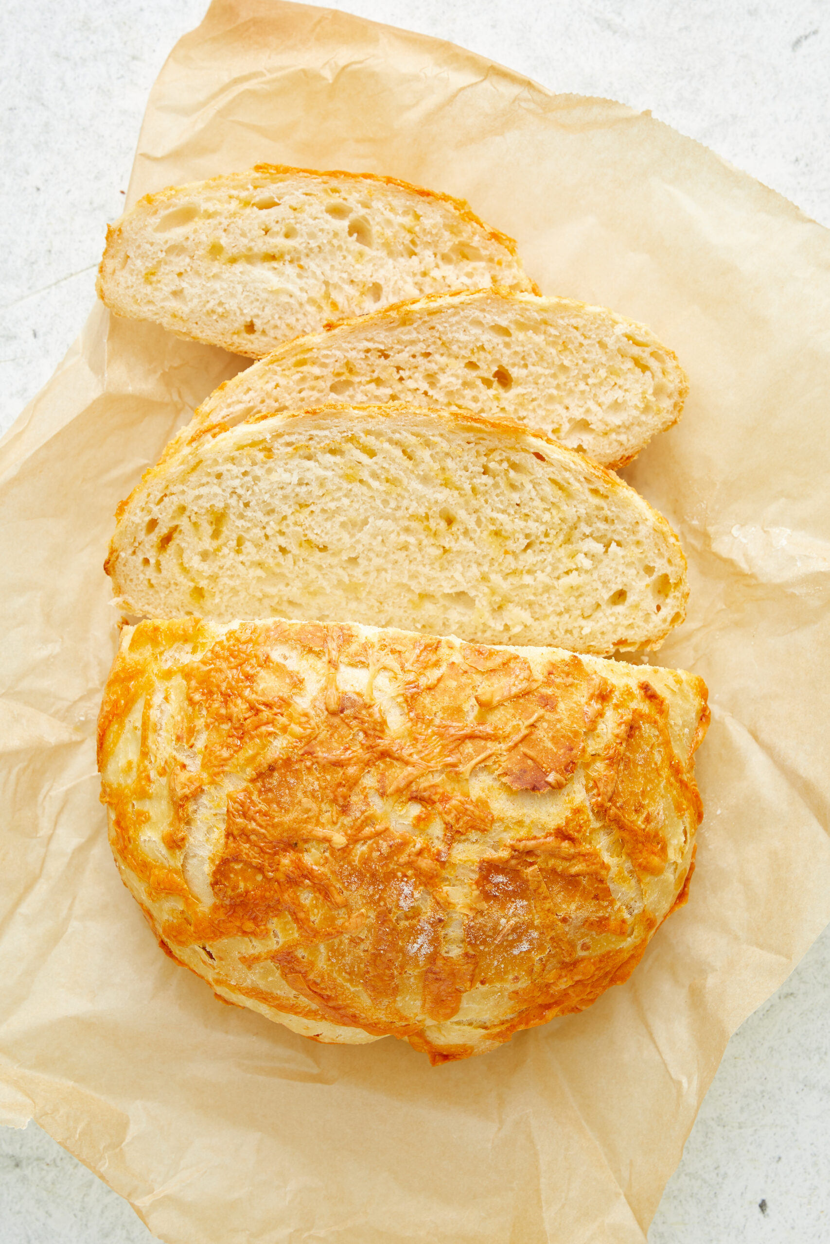 Slices of golden-brown cheese bread on parchment paper, showing the cheesy crust.