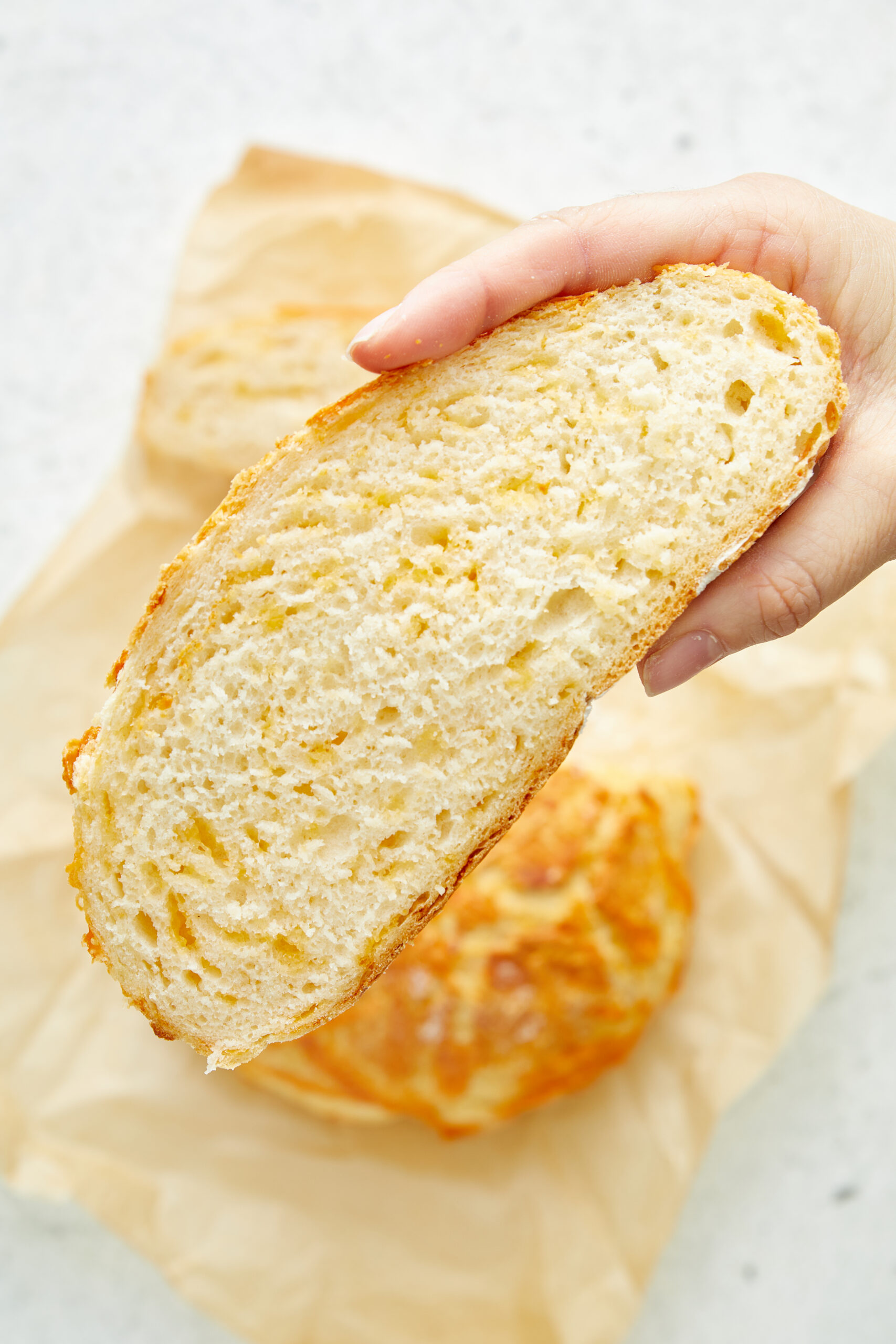 A hand holding a slice of cheese bread, revealing its soft, cheesy interior.