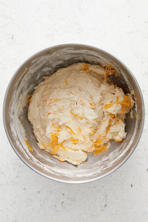Mixing shredded cheddar cheese into the sticky cheese bread dough.