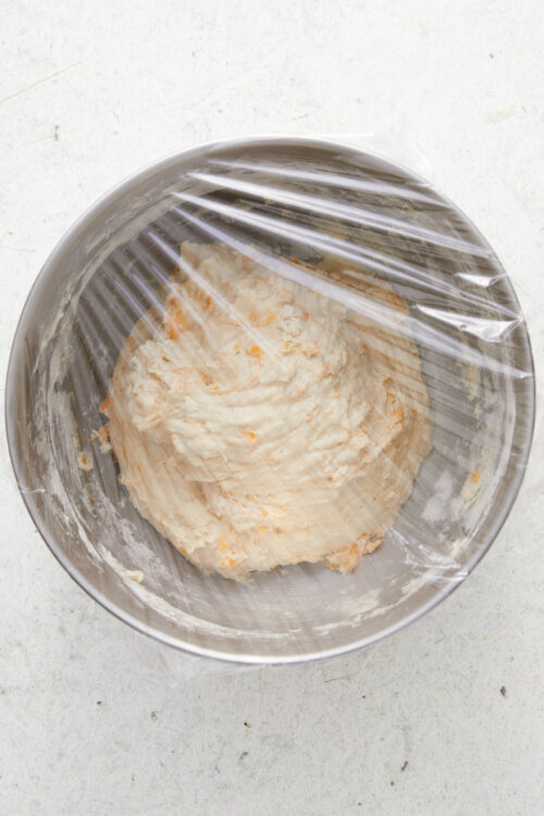 Covering cheese bread dough with plastic wrap to rest.