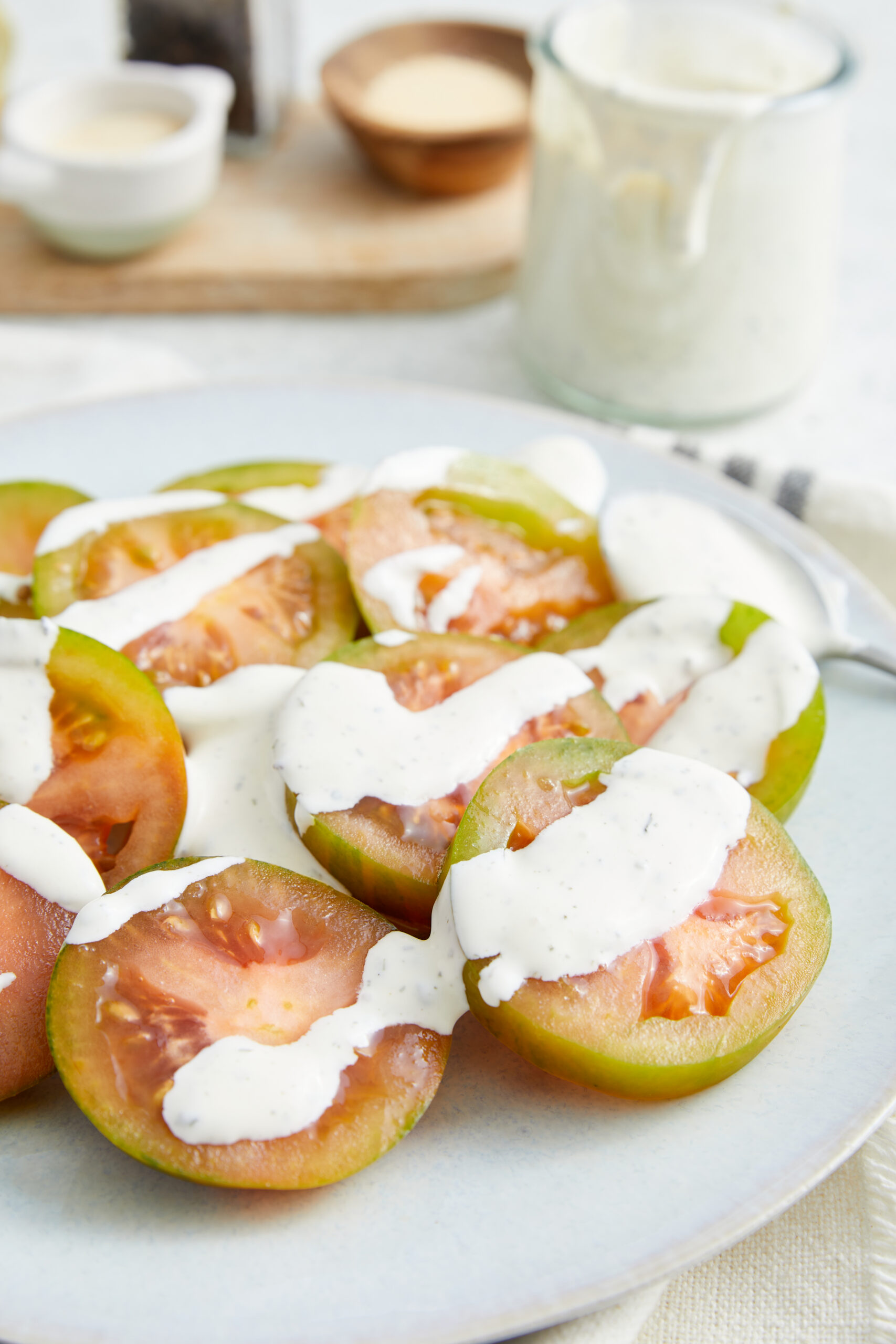 Homemade ranch dressing drizzled over sliced heirloom tomatoes on a white plate.