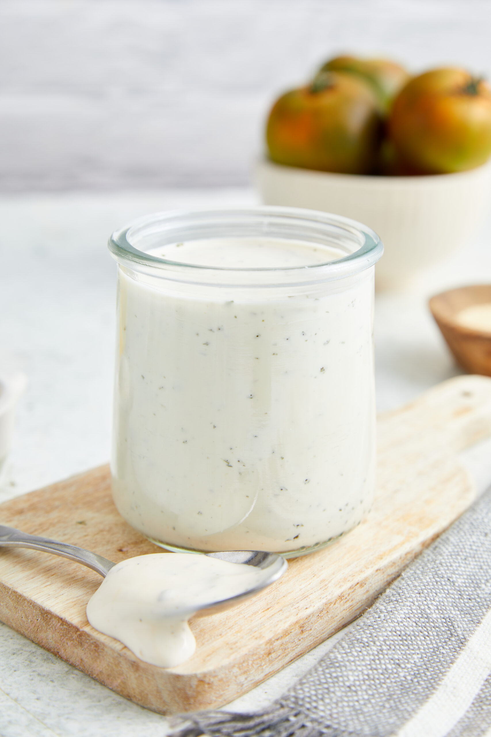 Homemade ranch dressing in a glass jar with a spoon on a wooden board.