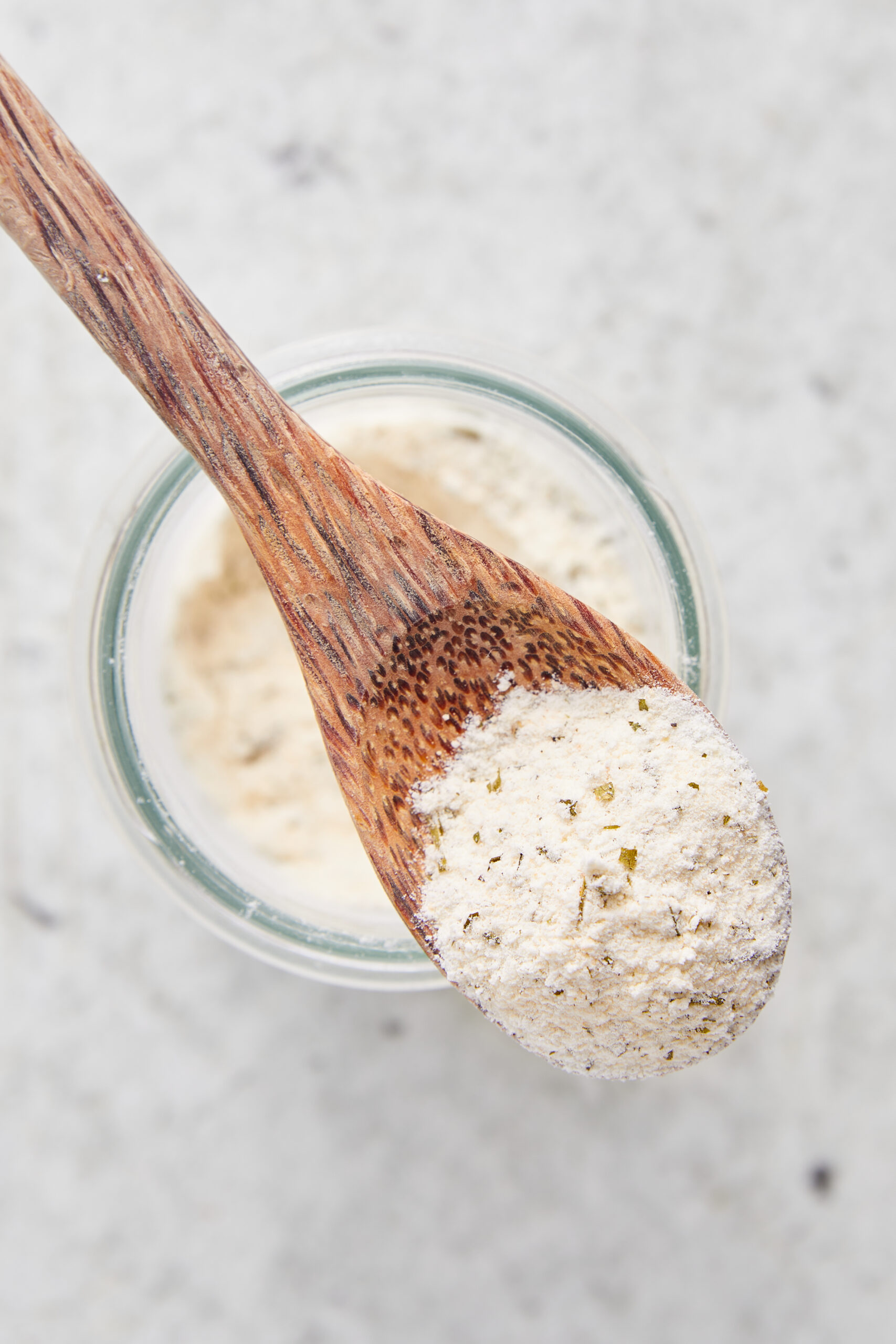 Homemade ranch seasoning, a white powder with green herbs, scooped from a glass jar.