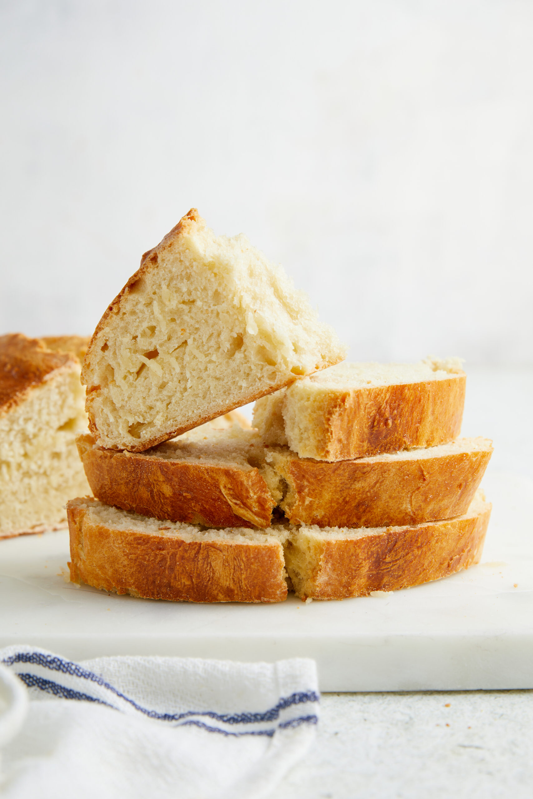 Slices of golden-brown Italian bread stacked on a white cutting board, with a soft interior.