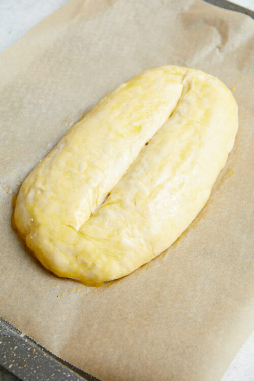 Unbaked Italian bread loaf, scored and brushed with egg wash.