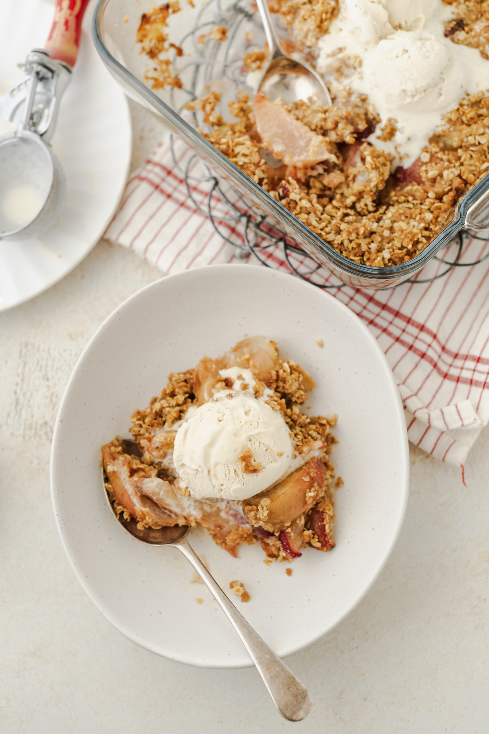 Peach crisp in a white bowl, topped with a scoop of vanilla ice cream.