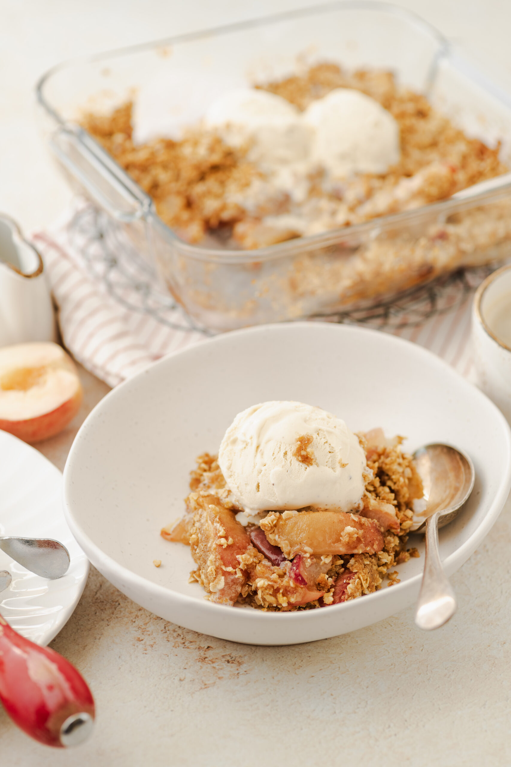 Peach crisp in a white bowl, topped with a scoop of vanilla ice cream.