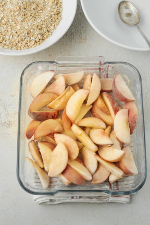 Sliced peaches in a glass baking dish for peach crisp.