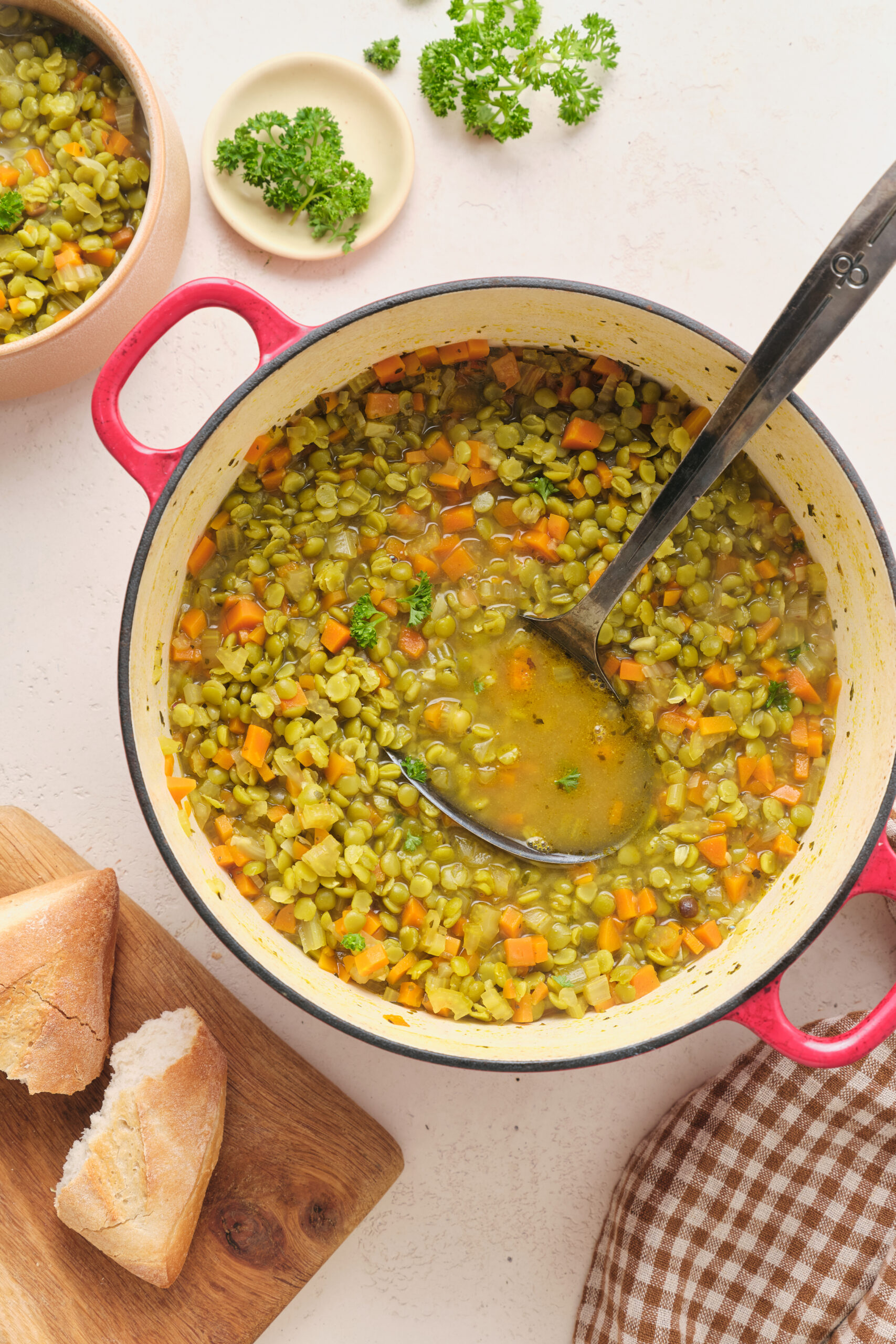 Vegan Split Pea Soup in a red pot, served with crusty bread and fresh parsley.