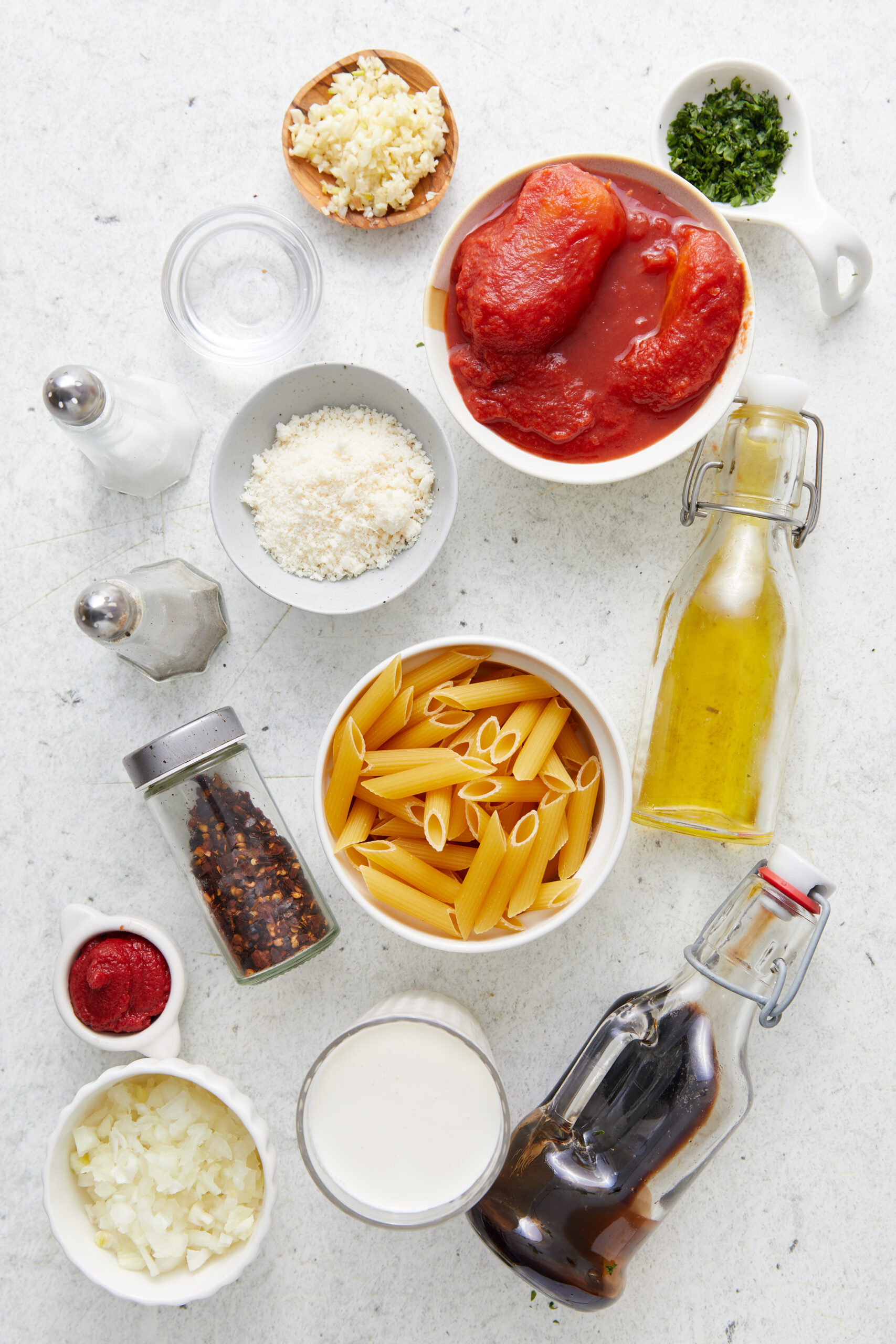 Ingredients for Vodka Sauce Recipe: penne pasta, whole peeled tomatoes, minced garlic, chopped onion, heavy cream, Parmesan cheese, and fresh basil.