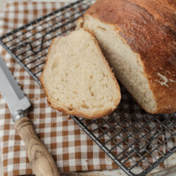 A freshly baked loaf of Artisan Bread, partially sliced, cooling on a wire rack.