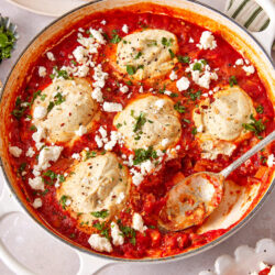 Vegan shakshuka in a white skillet, topped with vegan feta, cilantro, and crusty bread.