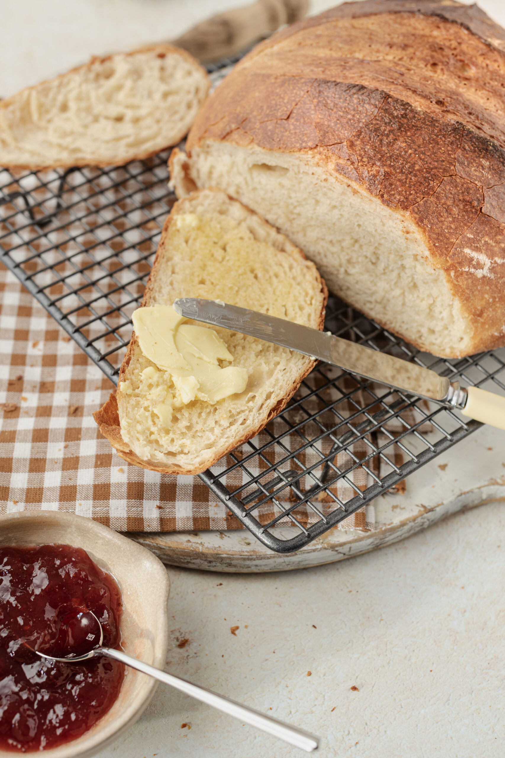 Freshly baked artisan bread, sliced and buttered, served with a side of jam.