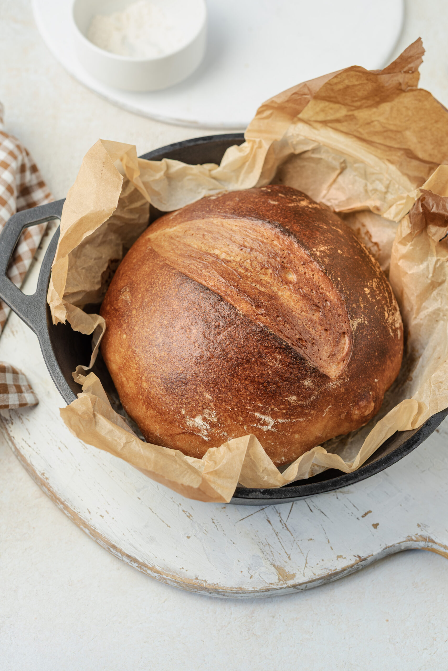 A freshly baked loaf of artisan bread in a cast iron pot, with a golden-brown crust.