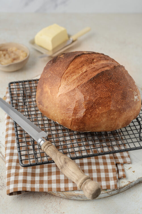 Artisan bread cooling on a wire rack with a knife and butter.