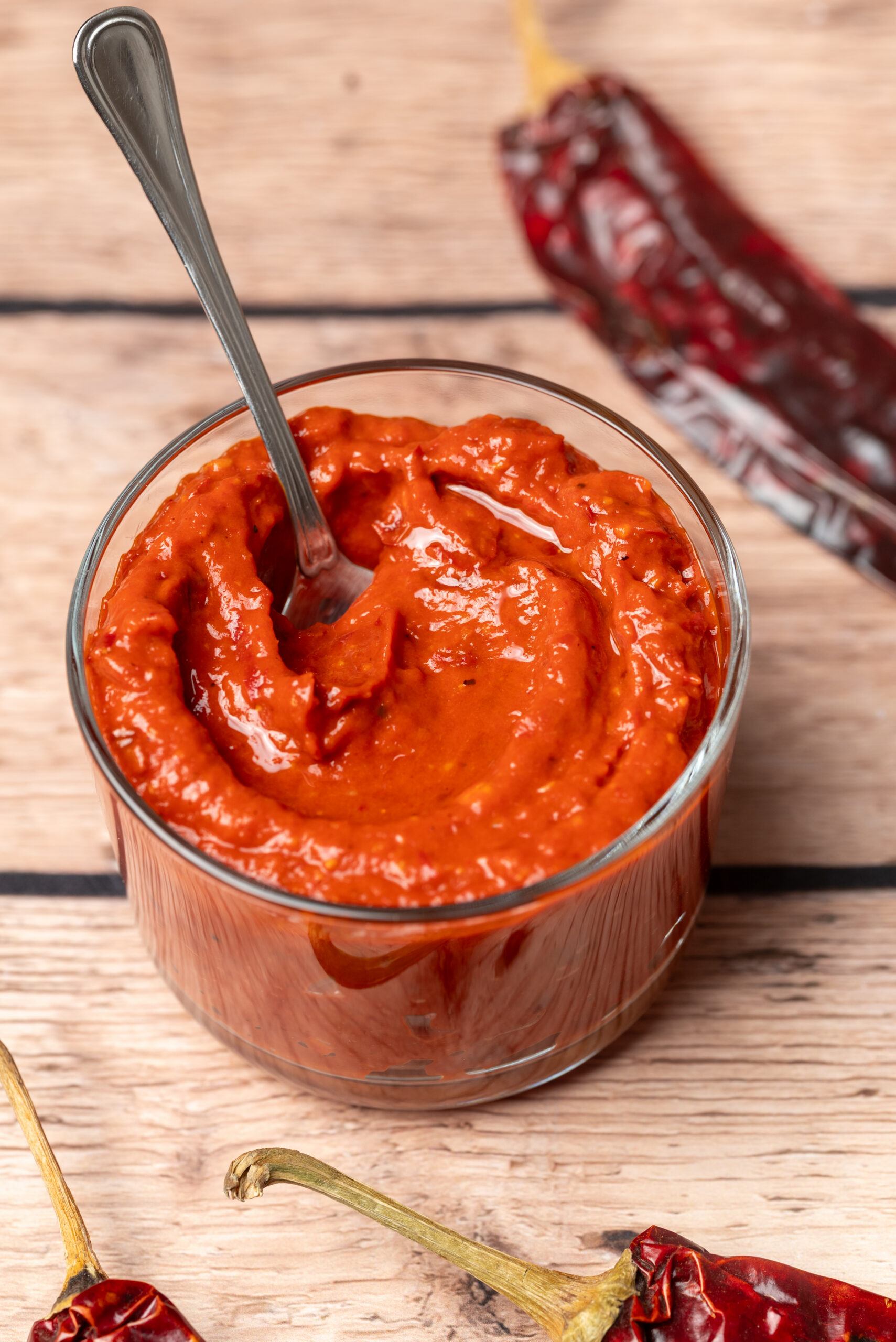 Homemade harissa, a vibrant red paste, in a glass bowl with a spoon.