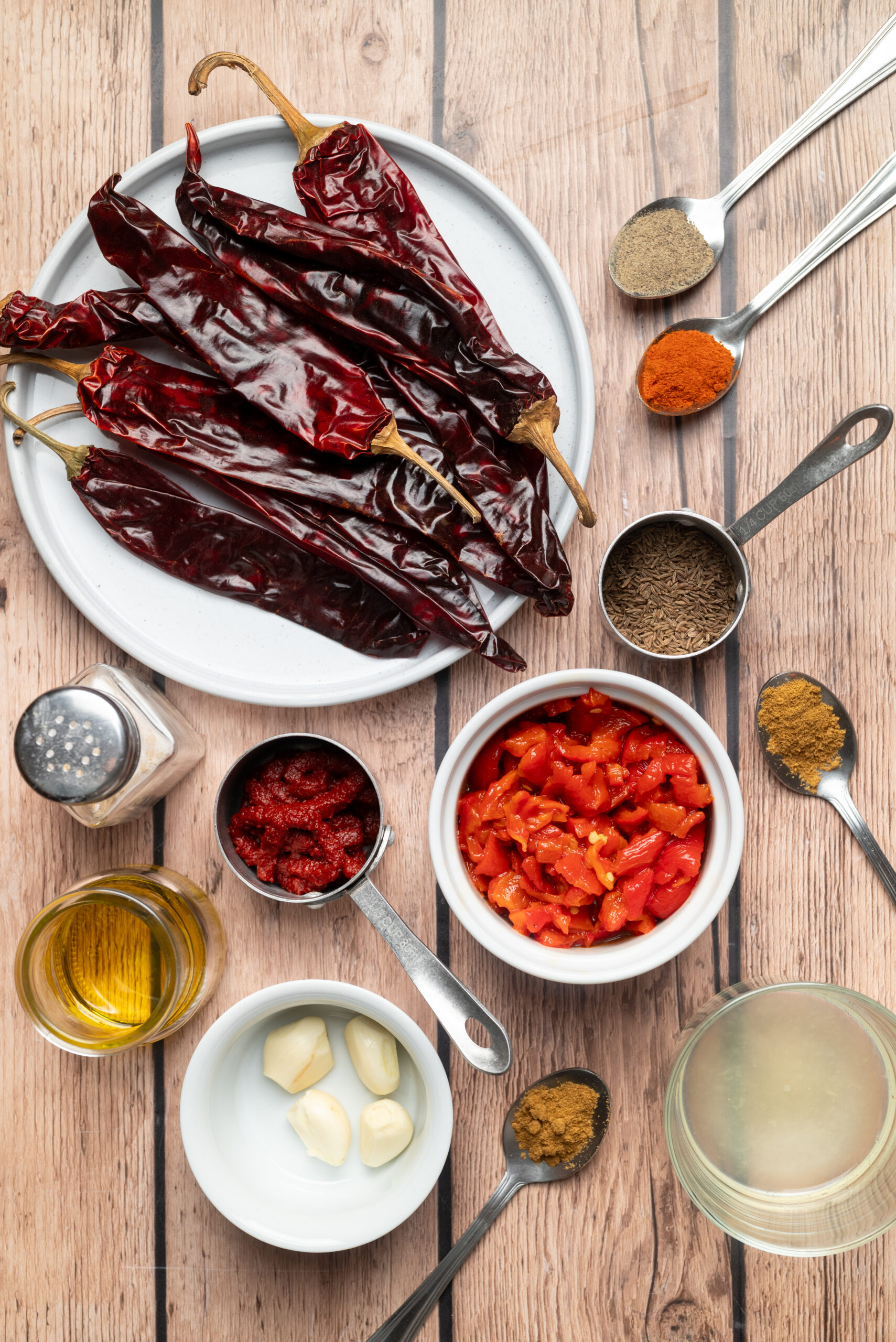 Ingredients for homemade harissa: dried chiles, roasted red peppers, tomato paste, garlic cloves, caraway seeds, ground cumin, and olive oil.