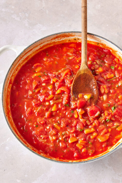 Stirring vegan shakshuka sauce in a white pot.
