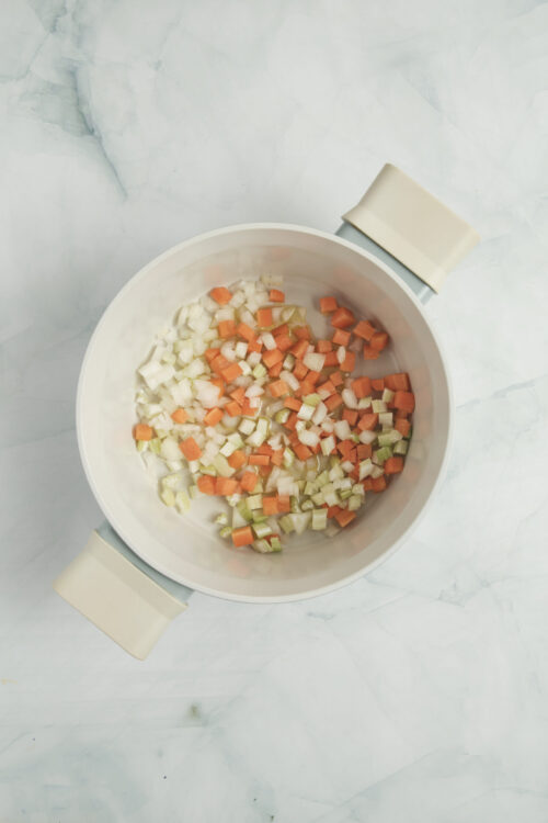 Cooking chopped onion, carrots, and celery in a pot for Vegetable Soup Recipe.