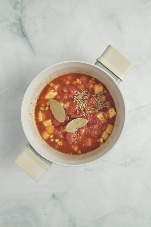 Adding tomatoes, broth, bay leaves, and herbs for Vegetable Soup.