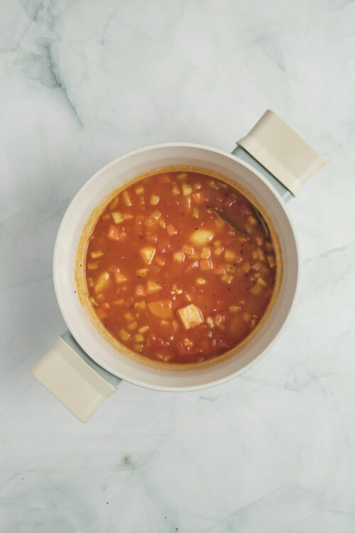 Vegetable soup simmering in a pot with diced vegetables.