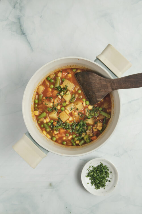 Vegetable soup in a pot, garnished with fresh parsley.